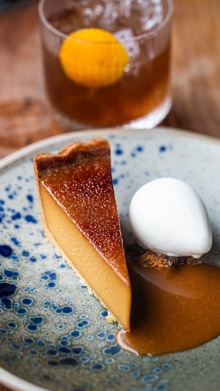 Slice of pumpkin pie with ice cream and sauce on a speckled plate.