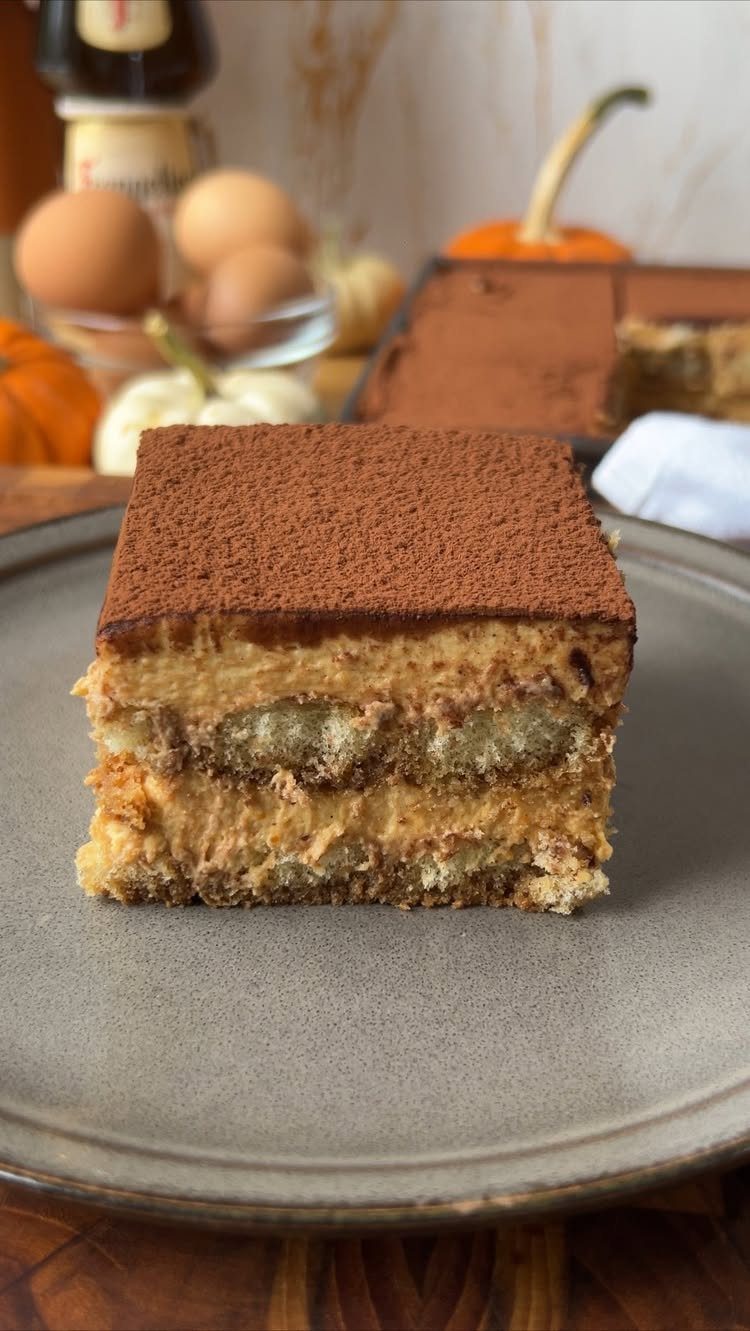 Slice of pumpkin spice tiramisu with cocoa powder on a grey plate.