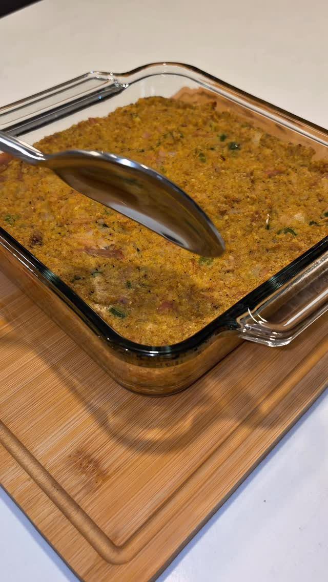 Golden-brown stuffing in a glass baking dish on a wooden cutting board.