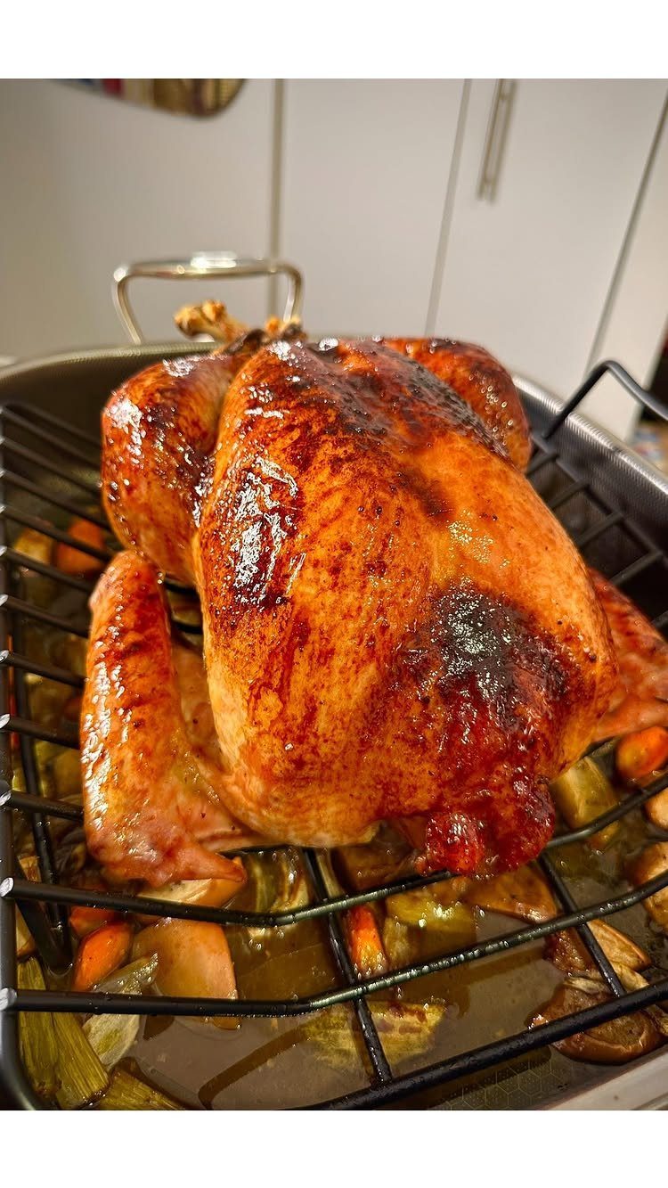 Roasted whole turkey with golden skin on a rack over roasted vegetables.