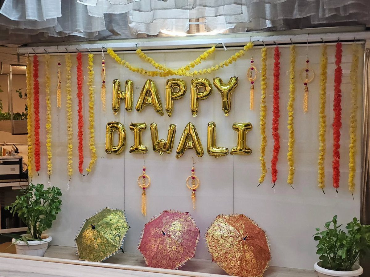 Gold Happy Diwali balloons and marigold garlands decorating a white office wall