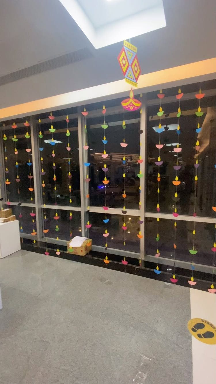 Colorful hanging paper diyas and ornaments decorating a glass wall in an office.