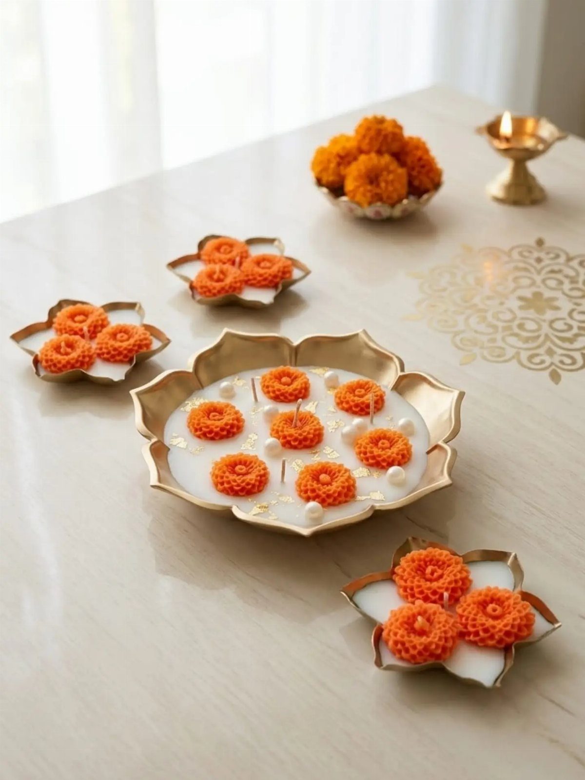 Gold urli bowl with floating orange marigolds and candles on a light surface