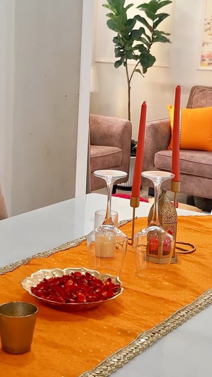 Orange fabric table runner with gold borders, red candles, and pomegranate seeds.