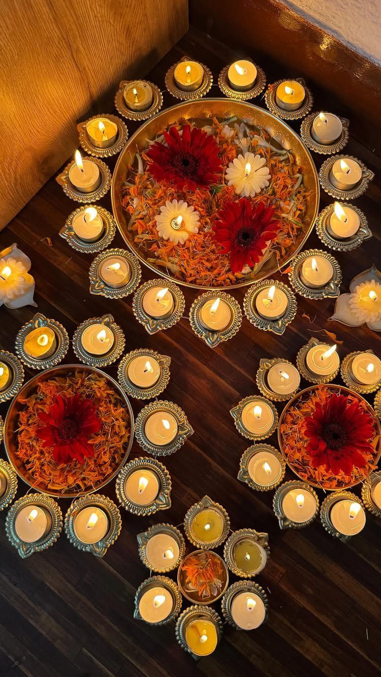 Golden bowls with flowers surrounded by lit diya lamps on a wooden floor.