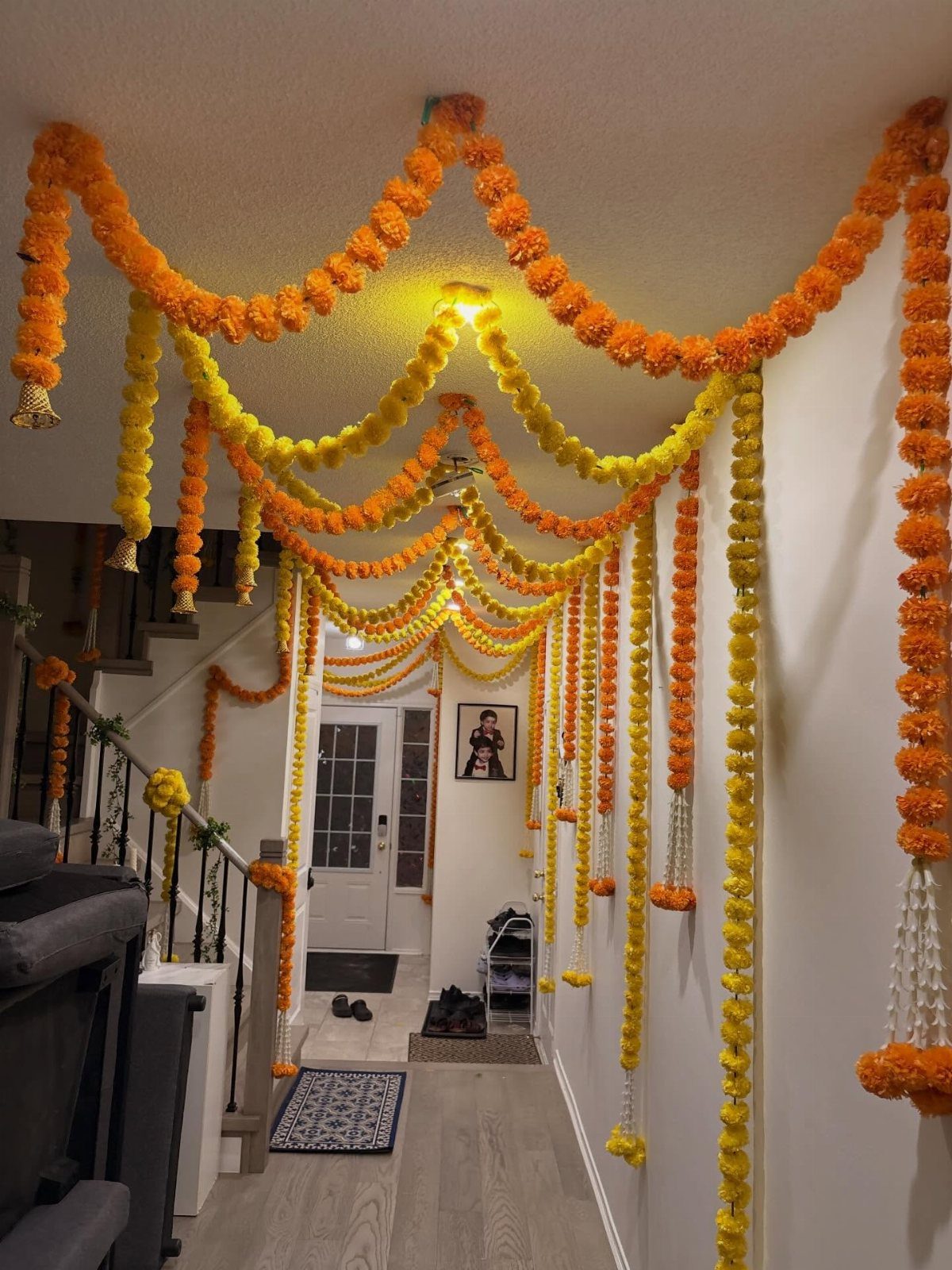 Orange and yellow marigold garlands draped across a ceiling in a home hallway.