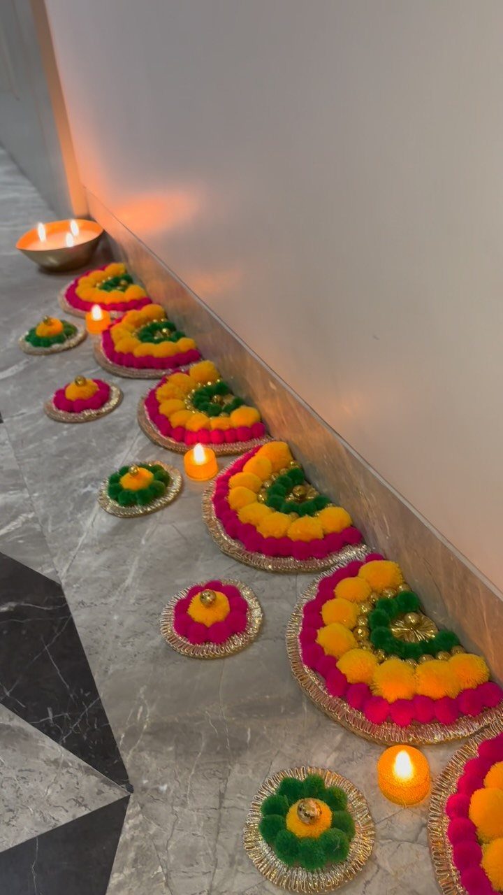 Colorful floral rangoli patterns with glowing diyas on a grey marble floor.