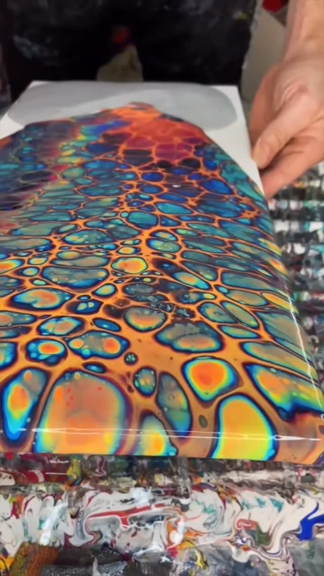 Acrylic pour painting with colorful cells on a canvas held by a hand