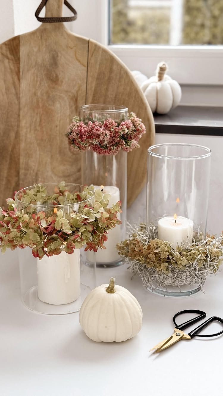 Glass cylinder vases with white candles and dried floral arrangements and white pumpkins.