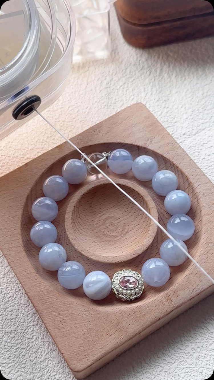 Beaded light blue stone bracelet with a pink charm on a wooden tray