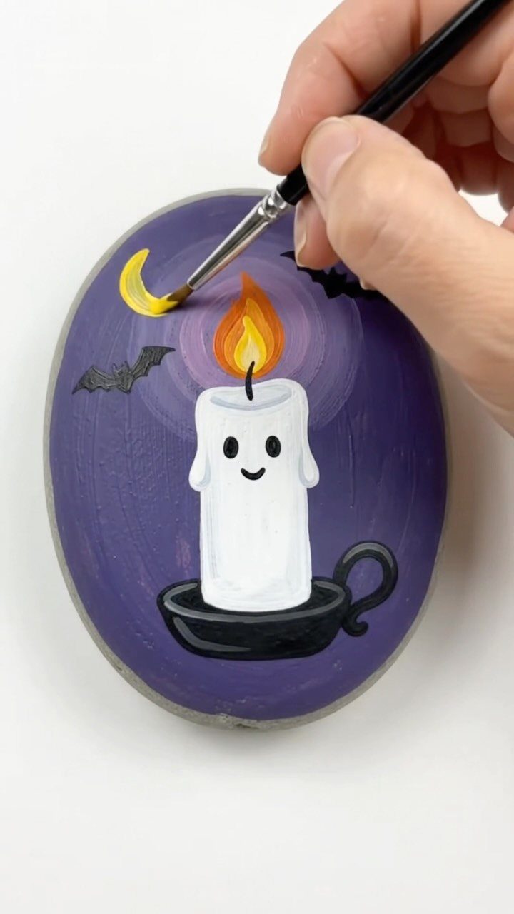 Hand painting a cute candle and bats on a purple smooth rock.