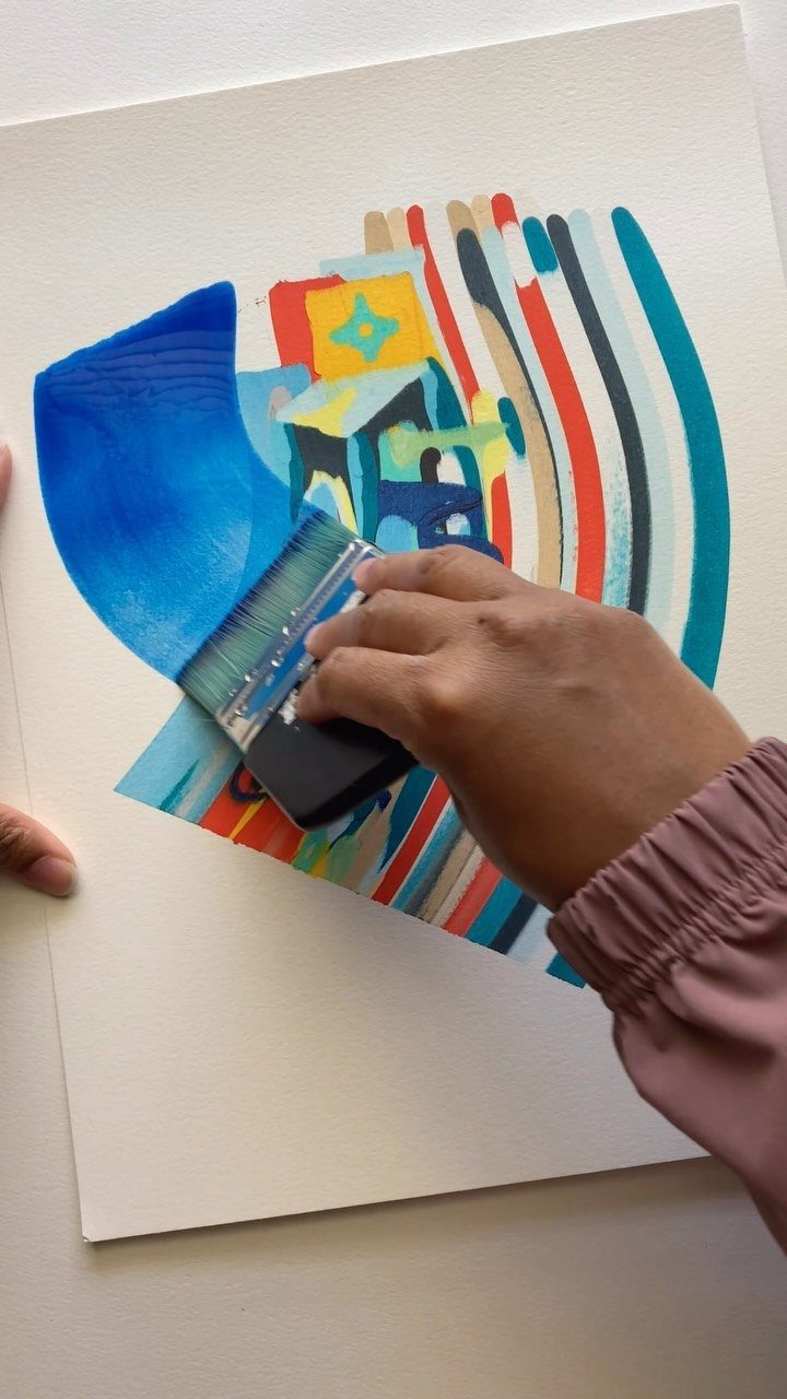 Hand using a small squeegee to create abstract colorful paint streaks on paper