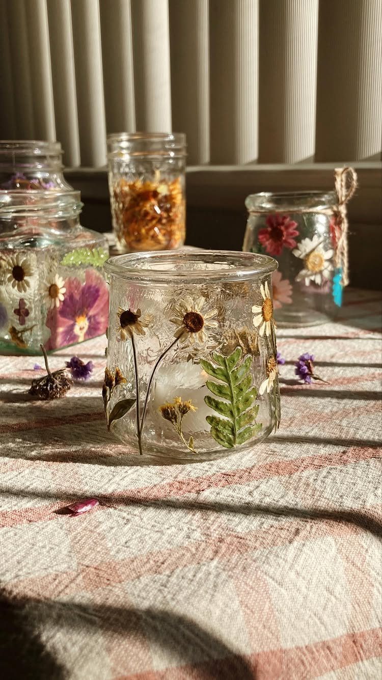 Glass jars decorated with pressed dried flowers and leaves on a checkered cloth.