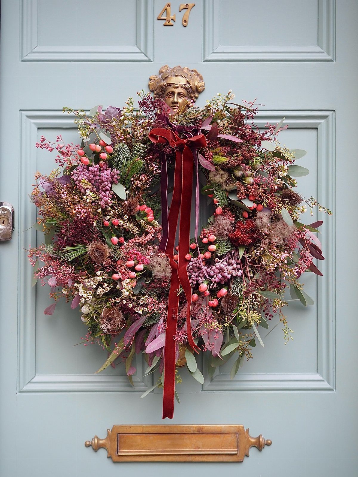 Floral wreath with red velvet ribbon hanging on a light blue front door