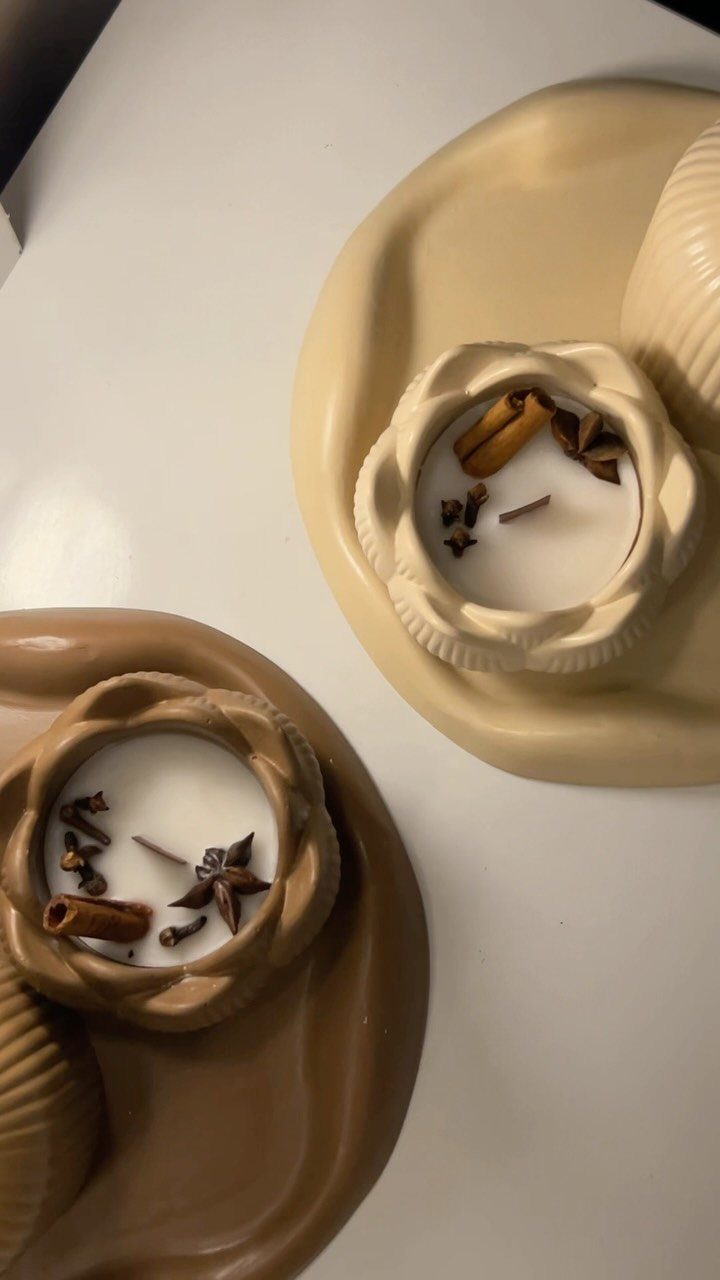 White candles in ceramic holders topped with cinnamon sticks and star anise spices.