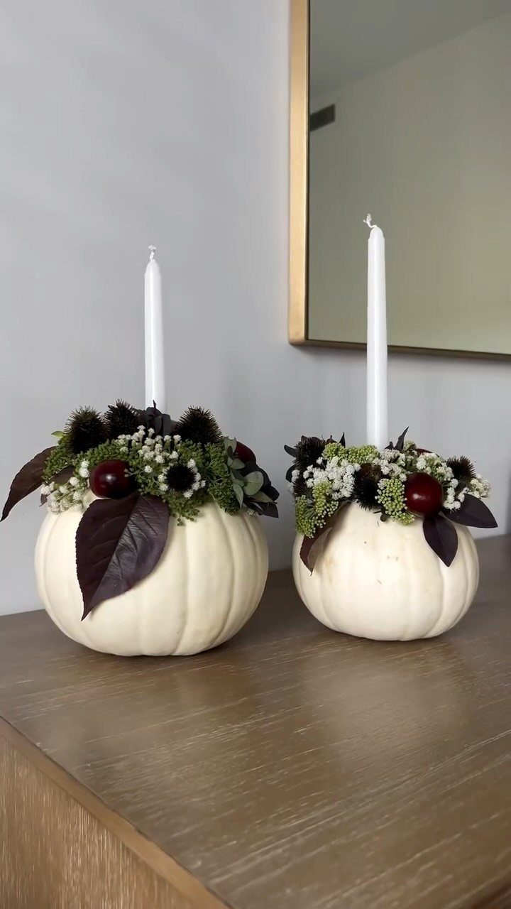 White pumpkins decorated with autumn foliage and berries holding white taper candles.