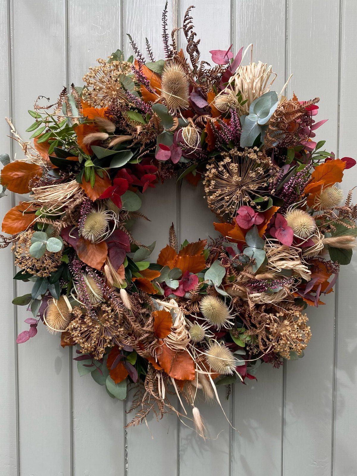 Dried flower wreath with autumn colors hanging on a grey wooden wall