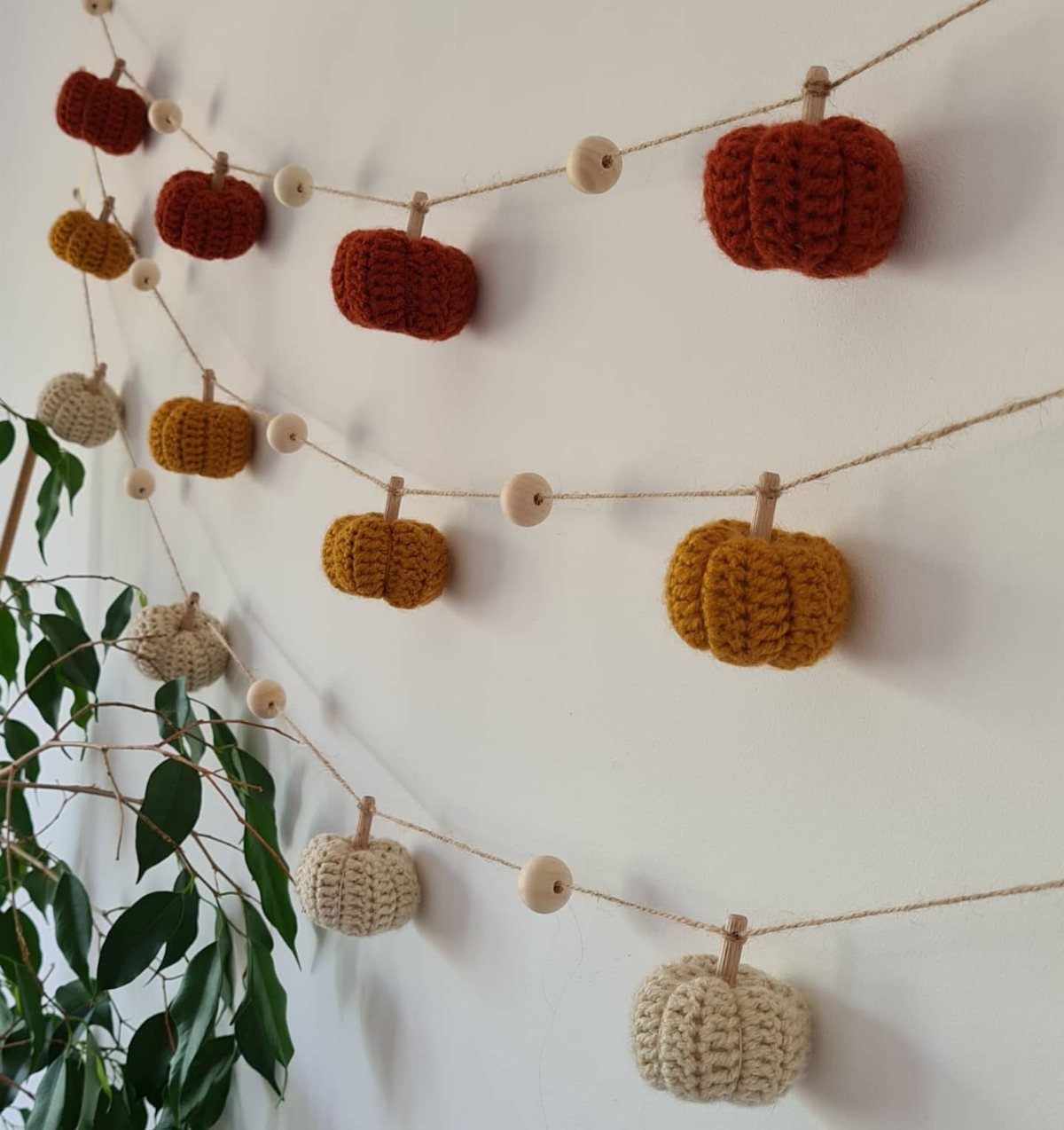 Crocheted mini pumpkin garland in autumn colors hanging on a white wall.