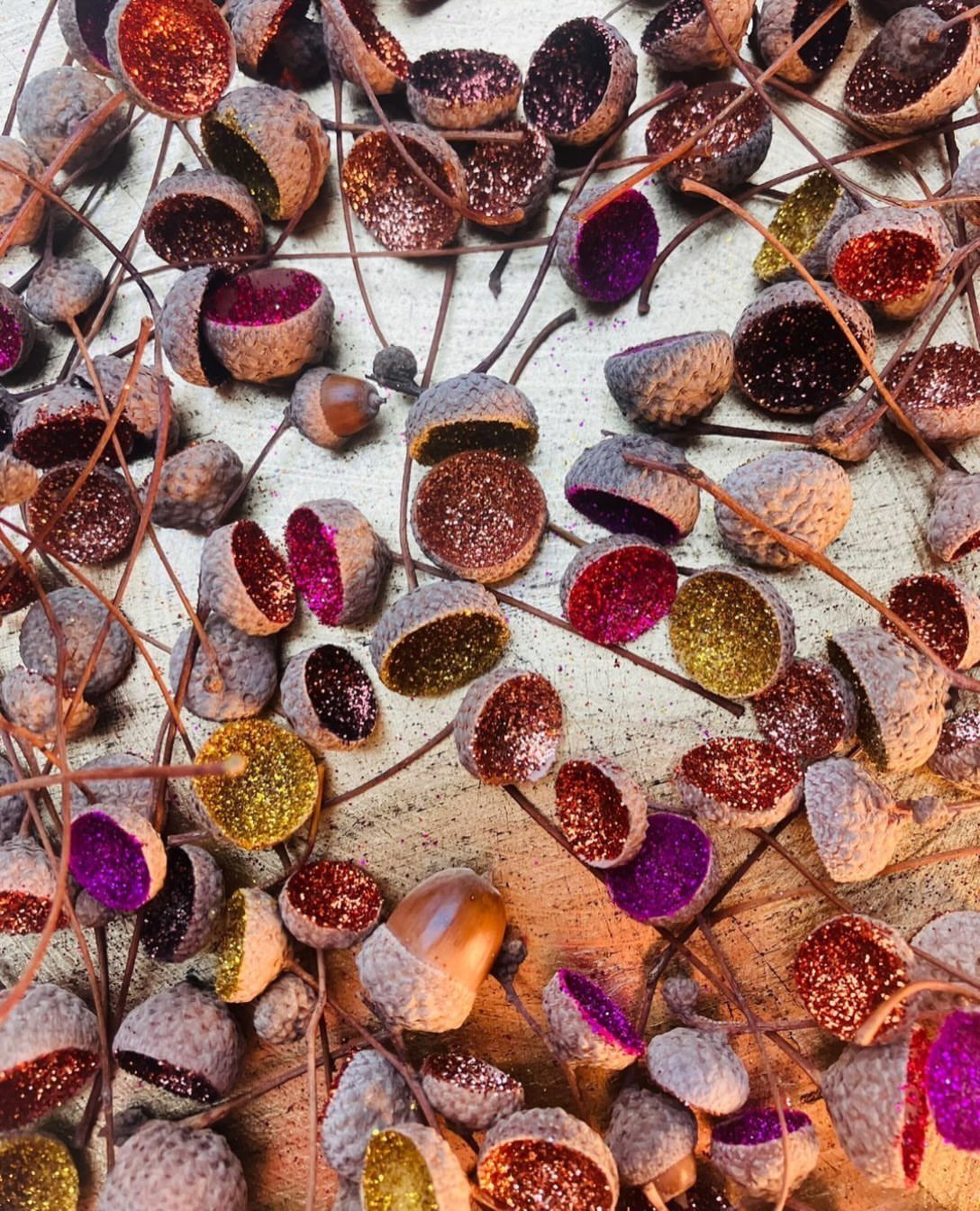 Glitter-filled acorn caps in gold, purple, and red scattered on a light surface.