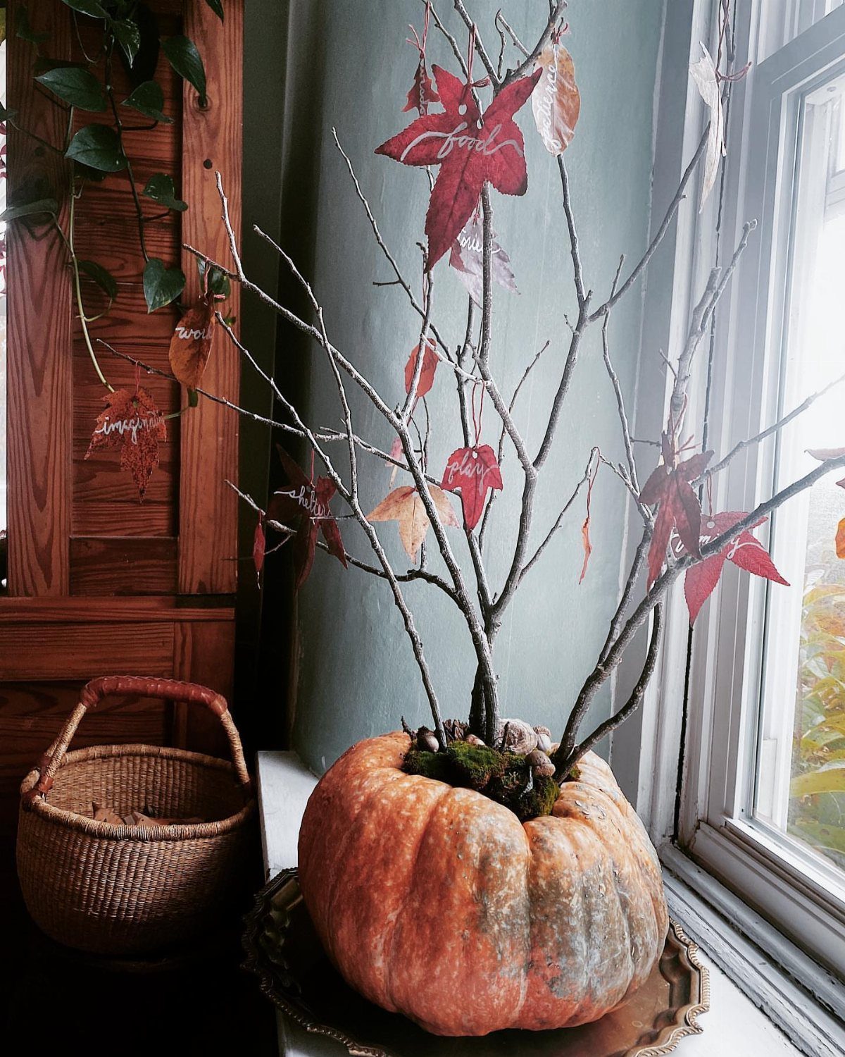 Bare branches with autumn leaves growing from a large orange pumpkin on a tray.