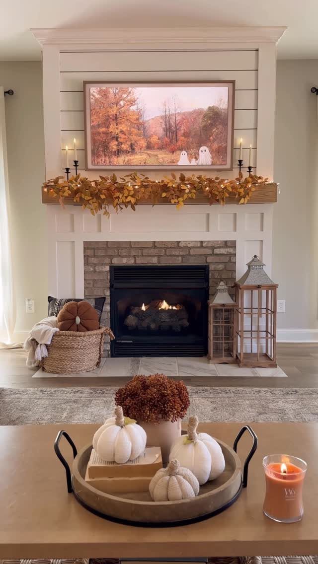 White fireplace mantle decorated with autumn leaves, candles, and a fall landscape painting.