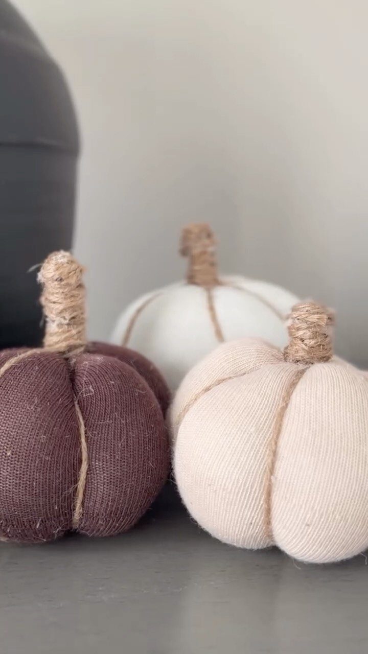 Three fabric pumpkins in burgundy and cream tied with twine on a grey surface.