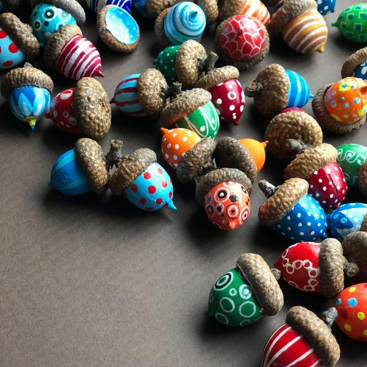 Painted acorns with colorful patterns scattered on a brown background.