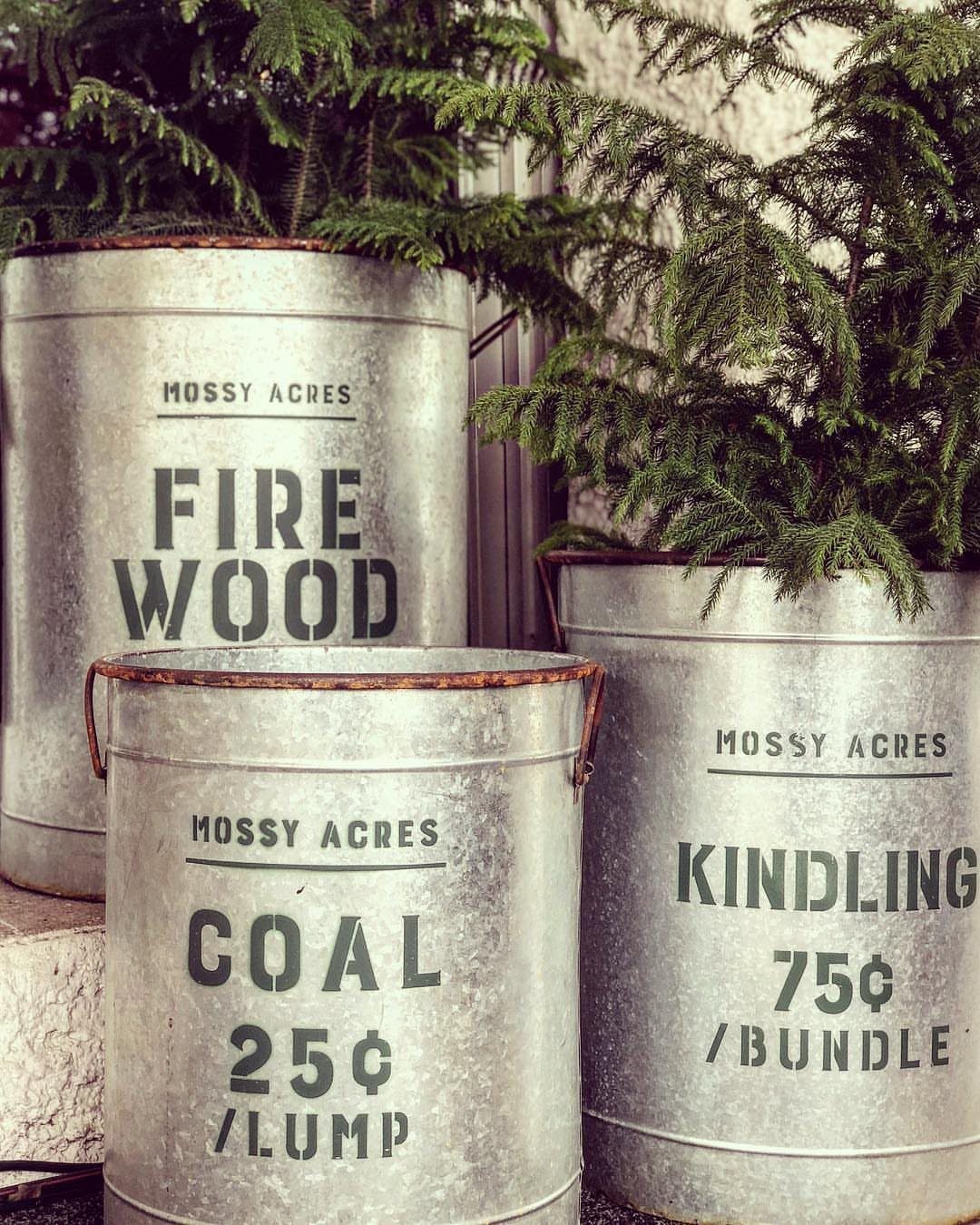 Galvanized metal buckets with vintage text holding green evergreen branches on stone steps.