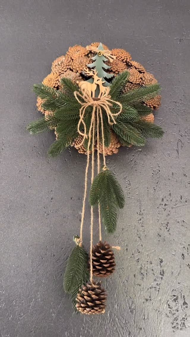 Pinecone wreath with evergreen branches, a wooden deer, and hanging pinecones on grey wall