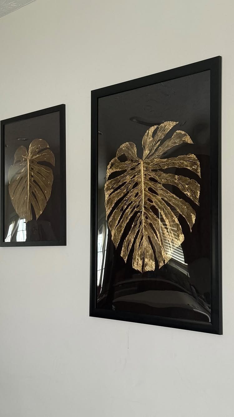 Gold monstera leaves pressed in black frames hanging on a white wall