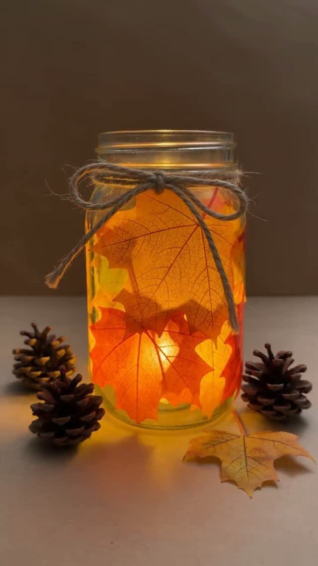 Illuminated mason jar decorated with pressed autumn leaves and tied with twine.