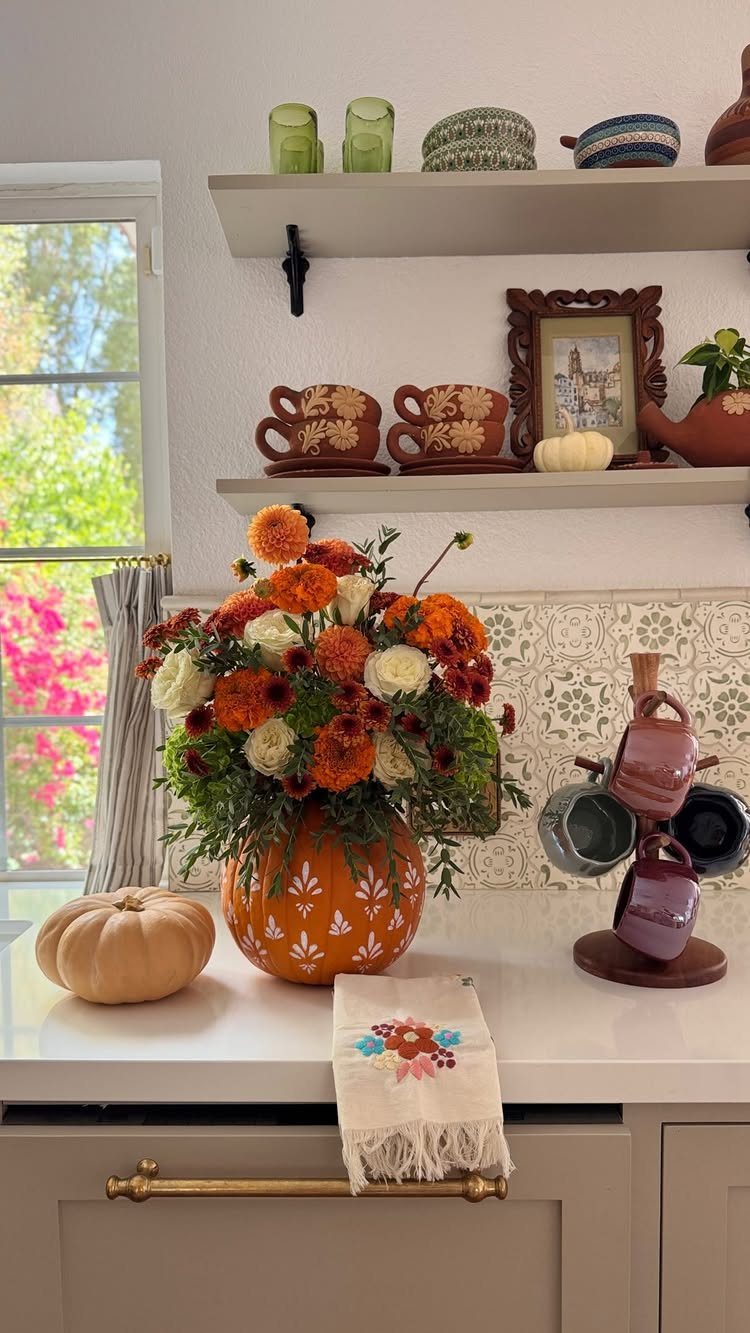 Pumpkin-shaped vase filled with orange and white autumn flowers on a white counter.