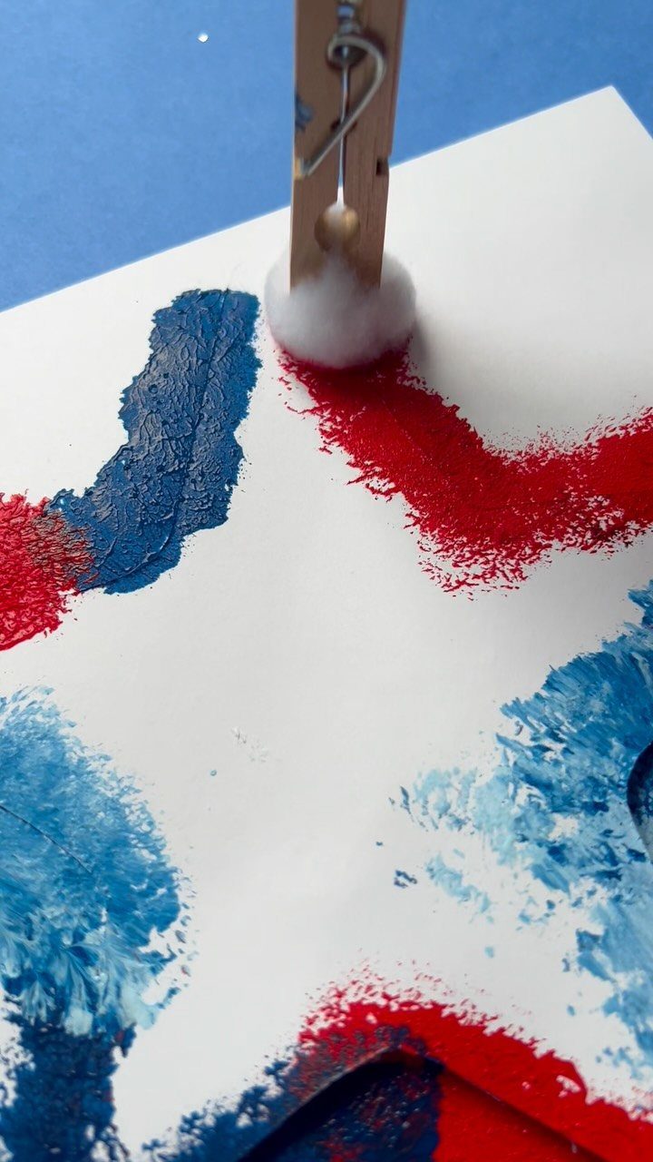 Cotton ball on a clothespin dabbing red and blue paint on white paper.
