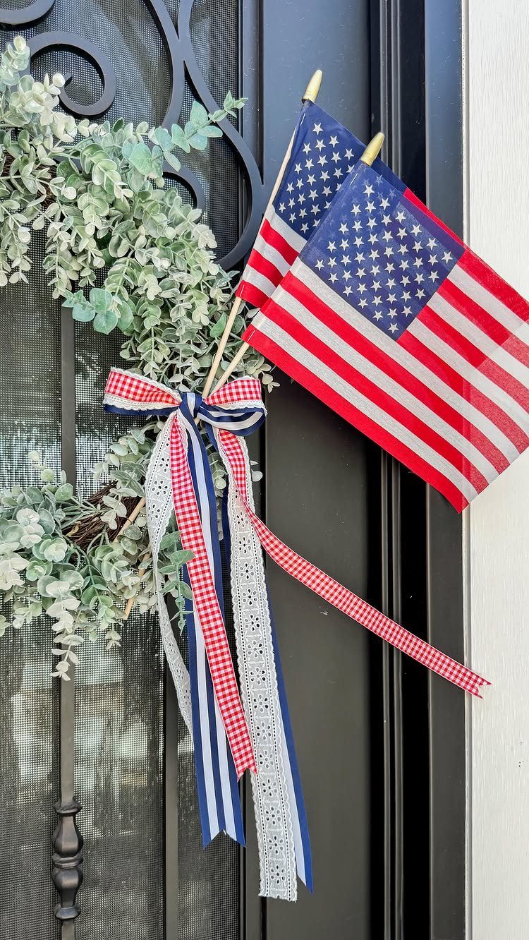 Green leafy wreath on a black door with American flags and patriotic ribbons.
