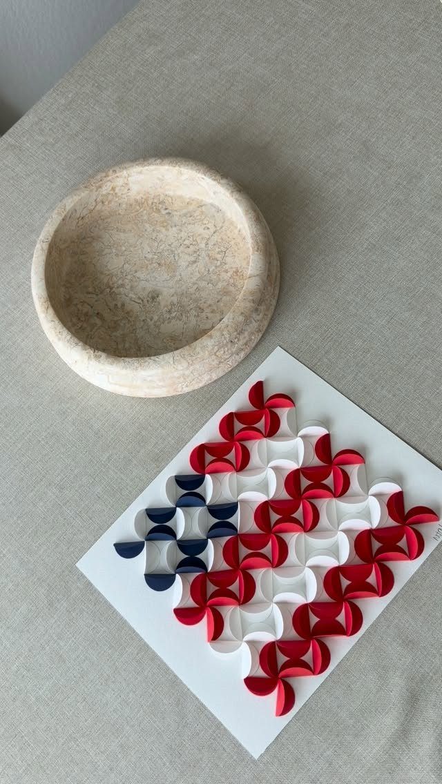 Red, white, and blue interlocking paper loop sculpture on a white square base.