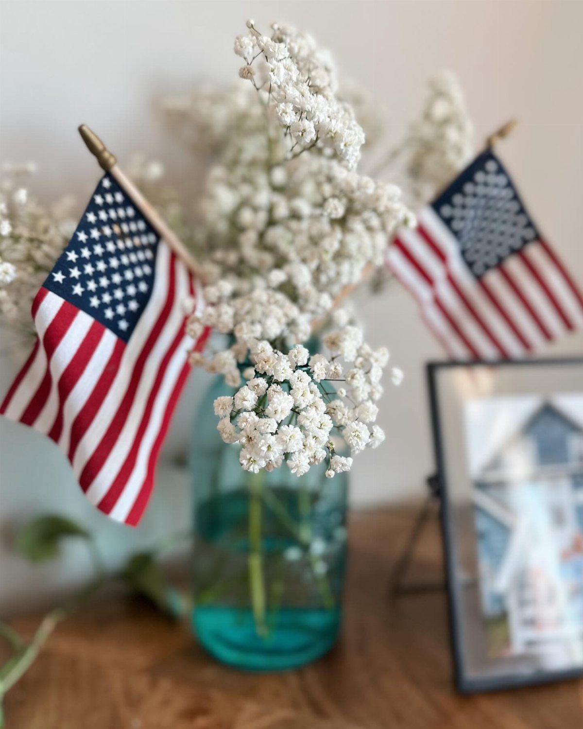 Blue mason jar with white flowers and small American flags on wooden table