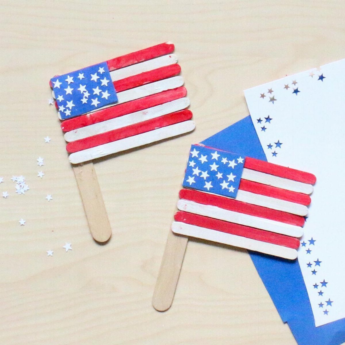 Two handmade American flags made from painted popsicle sticks on a wooden surface.