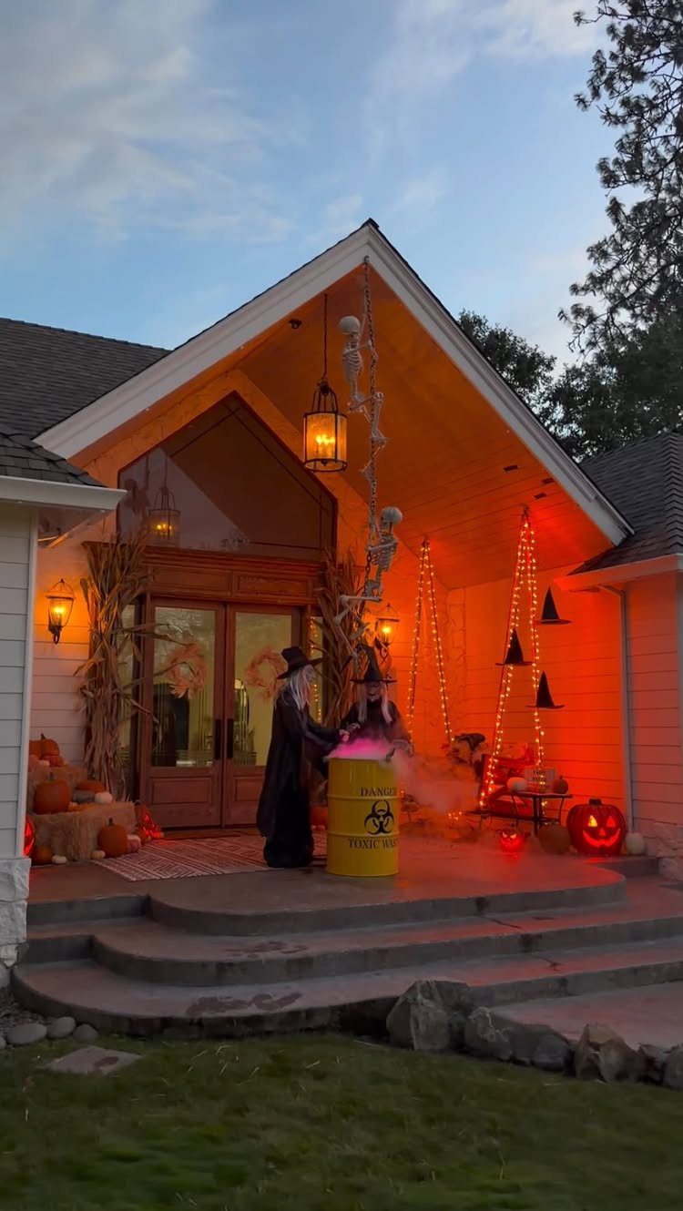 Two witch figures standing by a steaming yellow cauldron on a decorated porch.