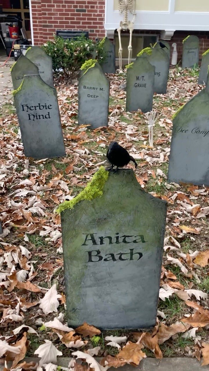 Grey DIY tombstones with funny names scattered across a leaf-covered autumn yard.