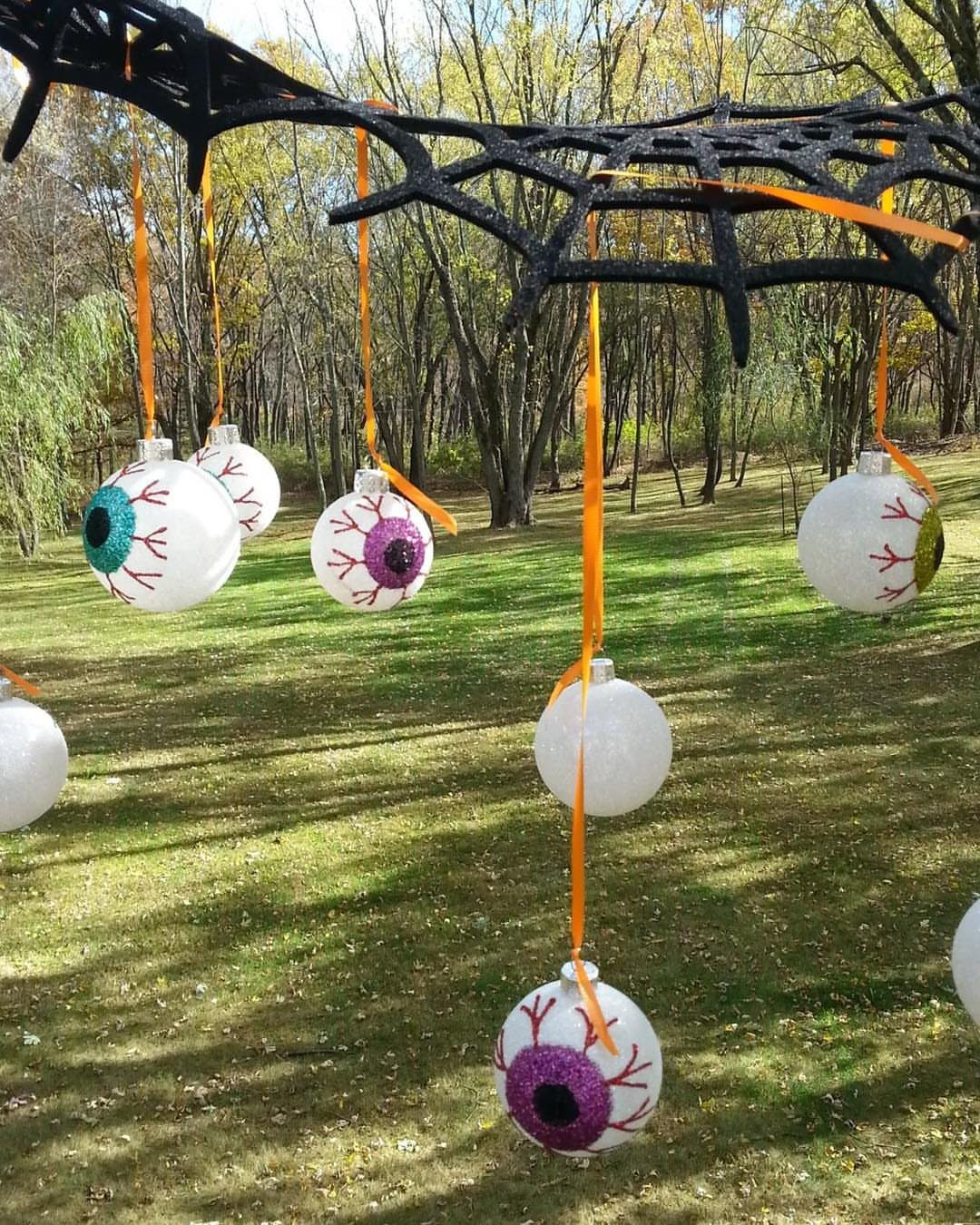 Eyeball ornaments hanging from a large black spider web in a grassy yard