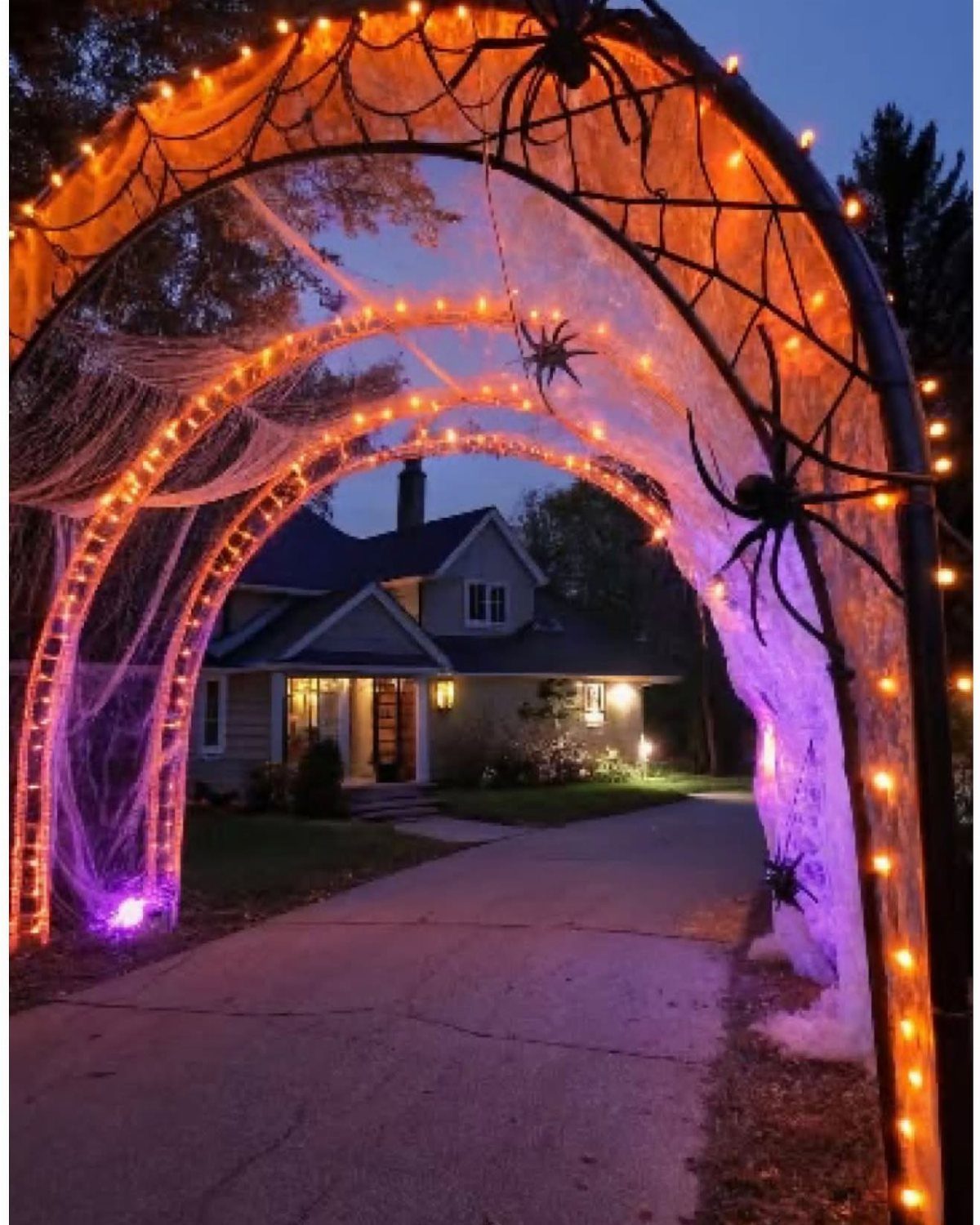 Spider web covered archway with orange lights and black spiders leading to a house