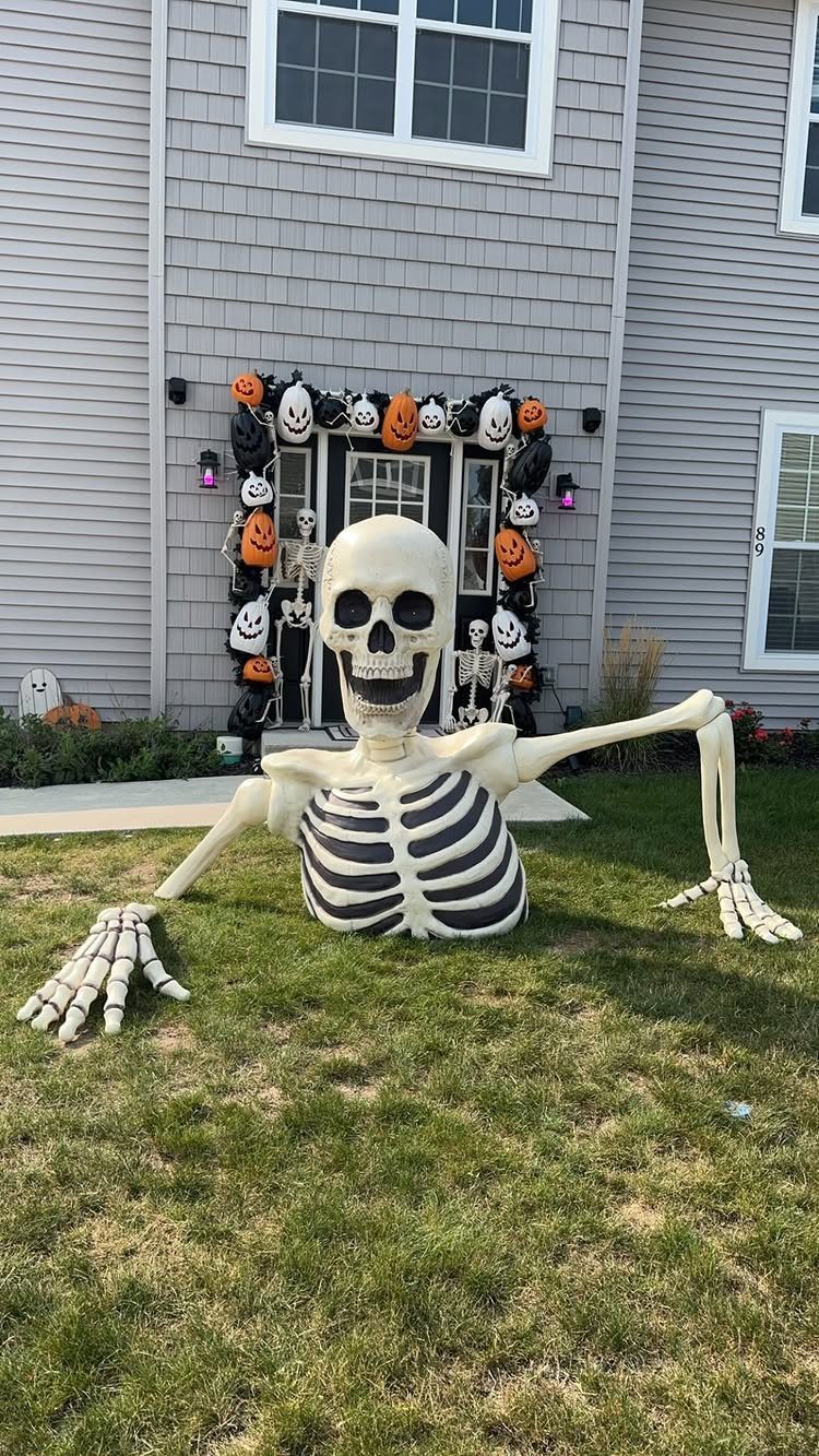 Plastic skeleton emerging from a grassy lawn in front of a decorated house.