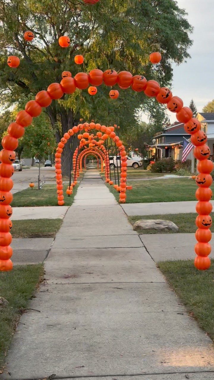 Orange pumpkin balloon arches lining a residential sidewalk for Halloween decorations.