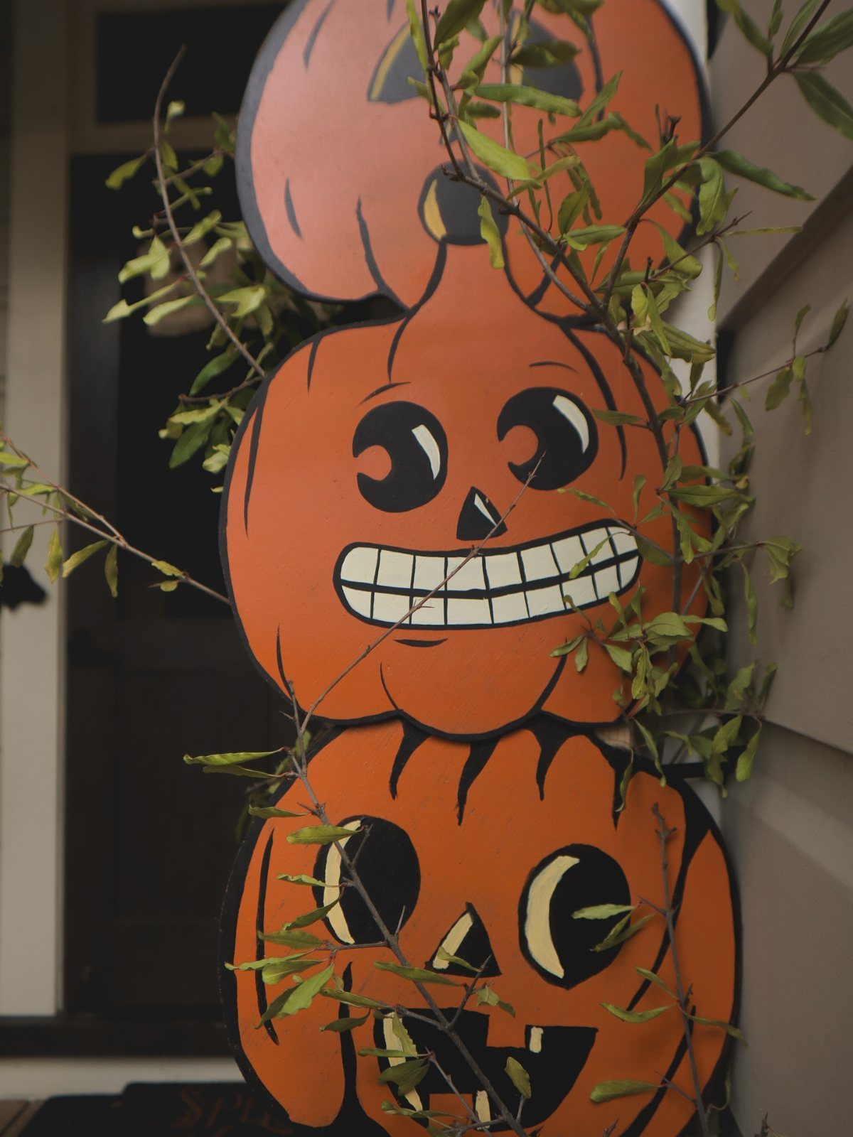 Stacked orange cartoon pumpkin cutouts with smiling faces among green leafy branches.