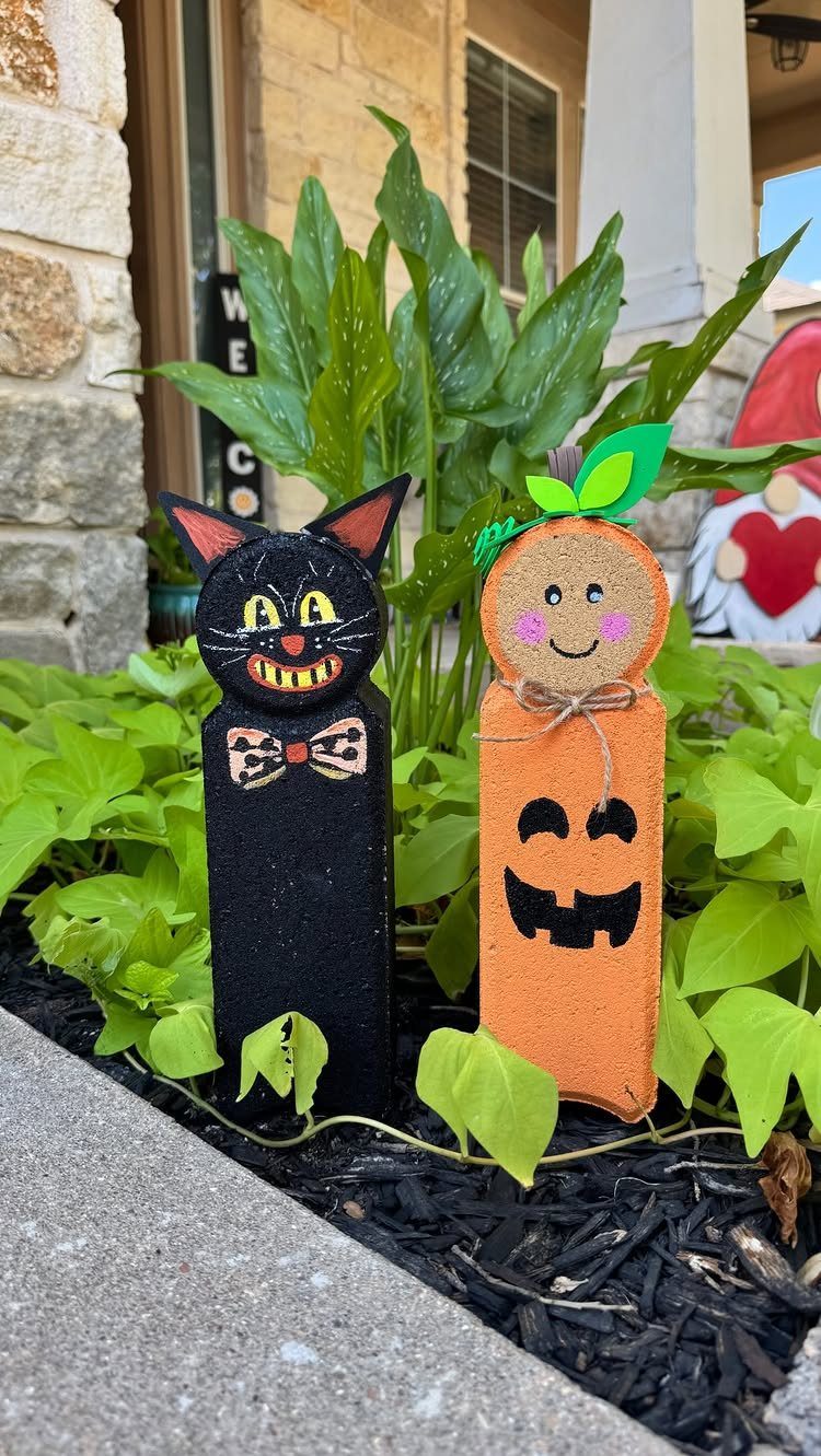 Black cat and orange pumpkin wooden garden stakes nestled in green garden foliage.