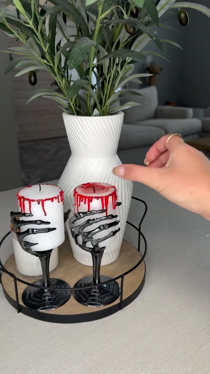 White candles with red dripping wax held by black skeleton hand holders.