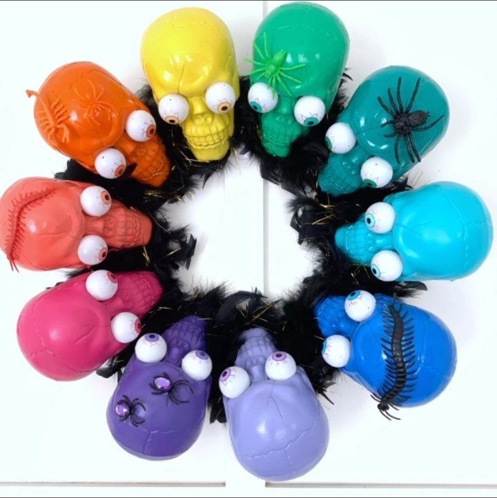 Colorful plastic skulls with googly eyes arranged on a black feather wreath.