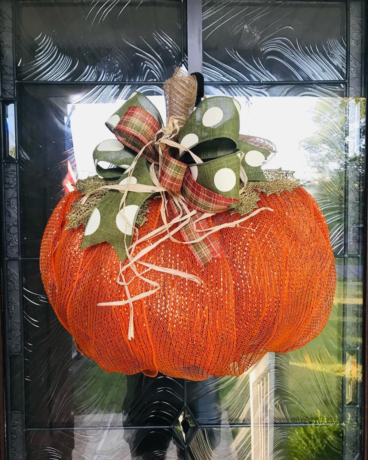Orange mesh pumpkin decoration with a large green and plaid bow on a door