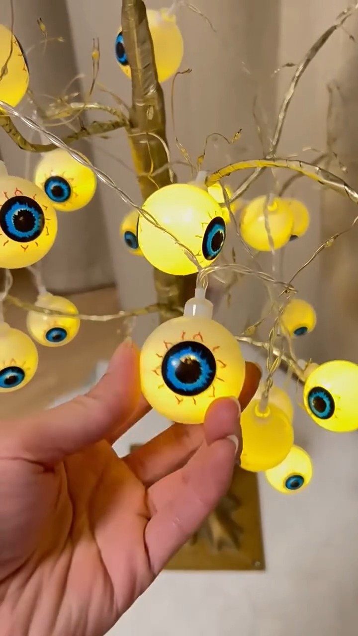 Glowing yellow eyeball lights strung on a gold decorative branch held by a hand.