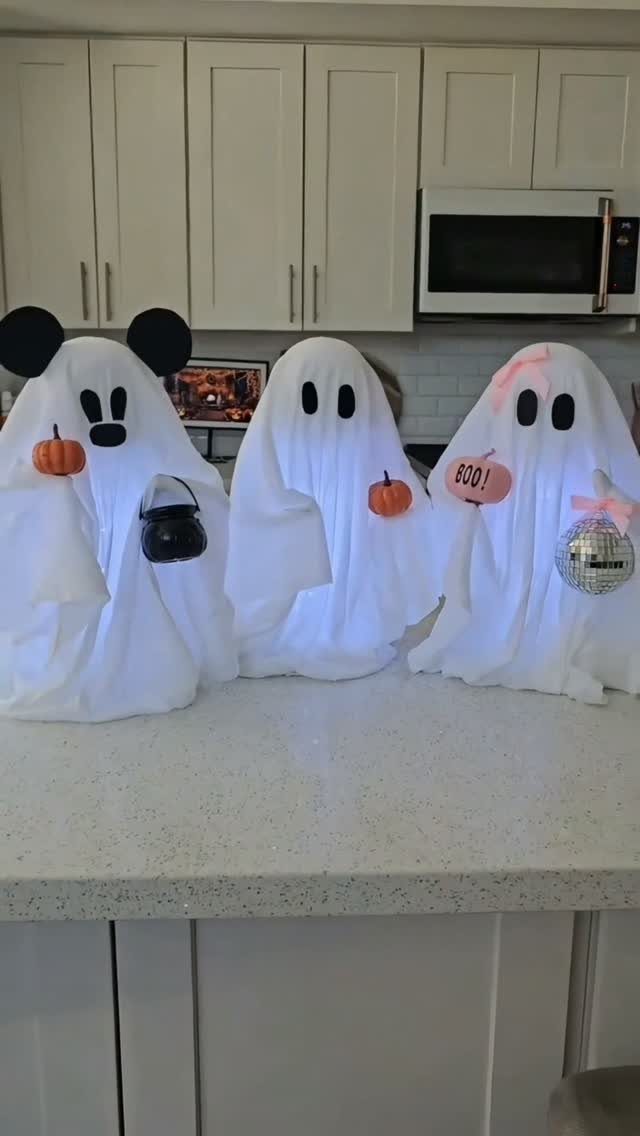 Three white fabric ghost decorations with accessories on a white kitchen countertop.